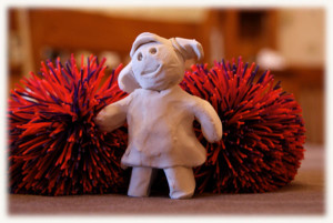 Clay figure of a girl in front of two pompoms 